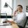 A cheerful call center agent wearing headphones works at a modern office desk