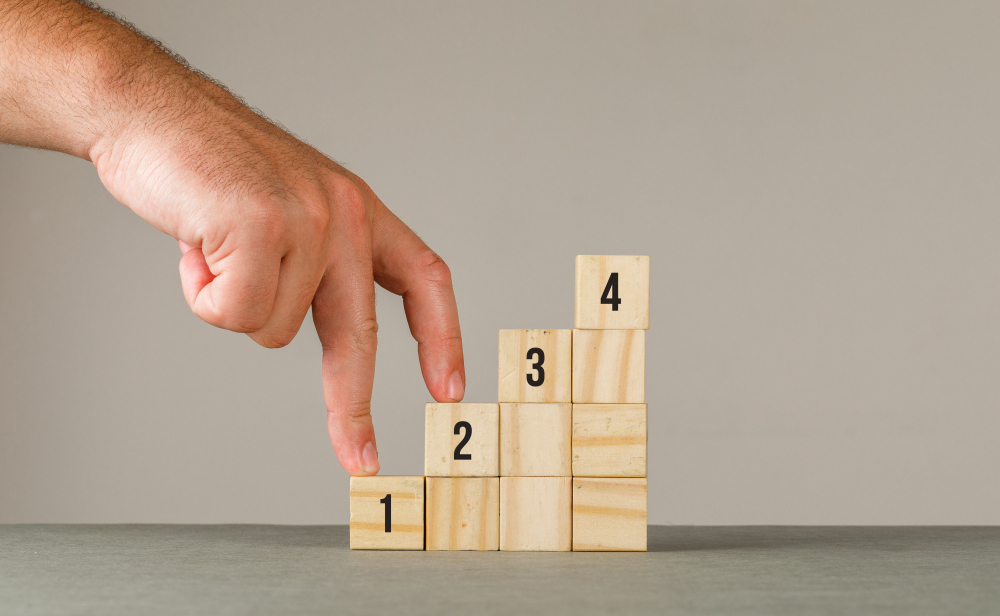 A hand points to a wooden block displaying numbers, emphasising the block's significance in the context